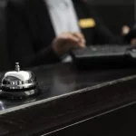 Paiements en Cryptomonnaie : Avantages et Limites à Connaître. Cloche sur un comptoir noir avec un concierge en arrière plan.